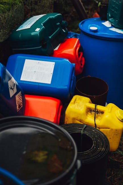 A top-down view of four large, cylindrical metal drums arranged outdoors on a concrete surface. The drums are painted in red with yellow tops, which show signs of rust, dirt, and weathering. Each drum